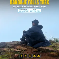 A trekker in a poncho sits atop a rocky outcrop on the way to Bandaje Falls, surrounded by fog. This is the moody beauty of a monsoon trek.