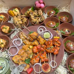 An abundant tandoori platter showcasing the variety we offer for barbecue events. This spread includes different types of chicken tikka, paneer skewers, and galouti kebabs, all served on a traditional clay platter with onion rings and lime.