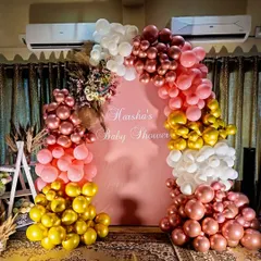 This personalized baby shower backdrop for "Harsha" showcases a vibrant balloon arch with rose gold, pink, yellow, and white balloons. We incorporated dried floral elements like pampas grass to add a touch of bohemian chic.