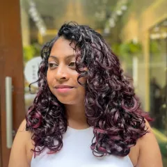 This vibrant Cherry Cola look was achieved with a no-bleach balayage. It’s a fantastic way to add a pop of rich red to dark hair while keeping curls juicy and defined.