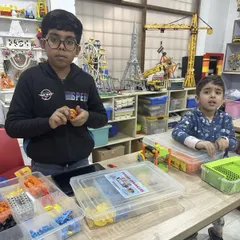 Two boys are deeply engaged in their LEGO projects at a table filled with building kits. The classroom setting, with large models in the background, shows the immersive world of engineering we create.
