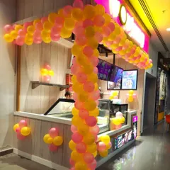 A custom balloon arch designed to fit the structure of a food kiosk for its opening day. The bright pink and yellow colors are cheerful and attract customers.