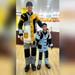 We believe in mentorship. An experienced shooter in full competition gear stands with a young student, symbolizing the passing of knowledge and inspiring the next generation to aim for the Olympics.