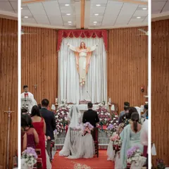 A wide shot of a Christian wedding ceremony, capturing the couple at the altar under the serene gaze of a statue of Jesus.