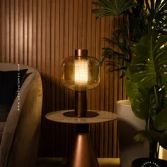 This elegant table lamp features a perforated inner core within a glass shade, creating a mesmerizing light pattern. Placed on a side table, it provides warm, decorative light that enhances the cozy atmosphere of a living room.
