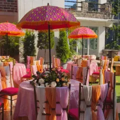 A colorful Mehendi setup for a destination wedding in Rishikesh. We used vibrant Rajasthani-style umbrellas, bright pink and orange chair drapes, and fresh floral centerpieces to create a festive atmosphere.