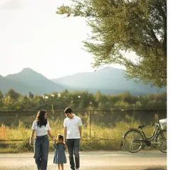 Holding hands, a family takes a leisurely walk down a path with mountains in the distance. The setting sun casts long shadows, capturing a simple, beautiful moment of togetherness during their outdoor family portrait session.
