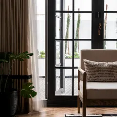 A detail shot showing the herringbone wood flooring and the simple, elegant lines of an armchair. The open French doors offer a glimpse of the outdoors, enhancing the breezy, coastal feel of the design.