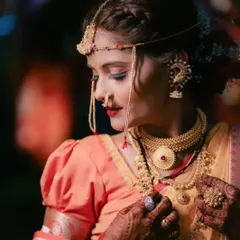 The final touches make all the difference. Here, a Maharashtrian bride adjusts her traditional jewelry, with her makeup perfectly complementing the rich gold tones.