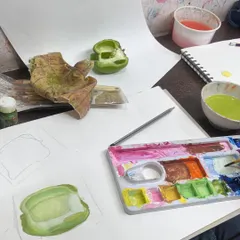 This workstation view shows the setup for painting a capsicum. You can see the real object, the initial sketch, and the palette with mixed greens, showing our hands-on process.