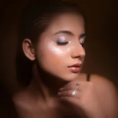This shot, with its warm, earthy tones, gives the glitter makeup a soft and glamorous feel. The focus is on the flawless skin and the gentle shimmer on the eyelids.