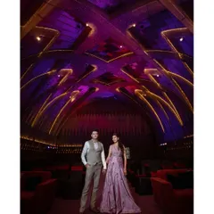 A stunning wide shot of a couple in a venue with incredible architecture and lighting. The vibrant purple and gold lights on the ceiling create a dramatic and unforgettable backdrop for this grand portrait.