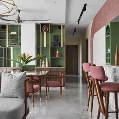 The living and dining area is defined by a unique color palette of sage green and dusty rose, with custom brass shelving for displaying art. The space flows into the breakfast bar, creating an open and social environment.