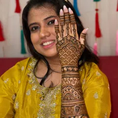 A smiling bride holding up her hand to show the detailed grid pattern on her bridal mehendi.