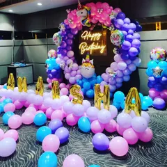 A magical unicorn-themed birthday party decoration. This setup includes a circular balloon arch in shades of pink, purple, and blue, unicorn foil balloons, and the birthday girl's name in foil letters.