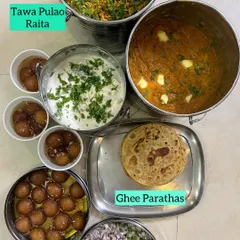 A complete meal featuring Tawa Pulao, Raita, buttery Pav Bhaji, Ghee Parathas, and Gulab Jamoon for dessert.