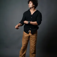 A three-quarter shot of a male model in a casual black shirt, captured in a dynamic pose as he rolls up his sleeves.