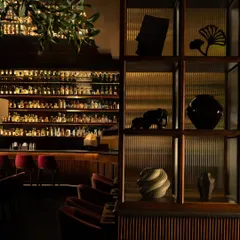 A detail of the shelving, filled with curated artifacts, set against the backdrop of the brilliantly lit bar. This composition creates a dialogue between intimate objects and the grand scale of the space.