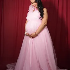 A full-length view of the one-shoulder pink maternity gown. Its long, flowing design is very flattering and creates a soft, elegant silhouette.