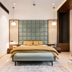 A serene and symmetrical master bedroom design. The large, quilted sage-green headboard is the centerpiece, flanked by elegant pendant lights that provide warm reading light.