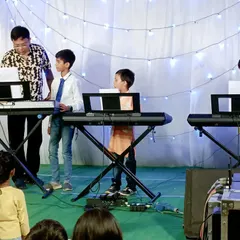 An instructor guides his young keyboard students during a live stage performance. We are right there with our students, supporting them as they share their talent with the audience.