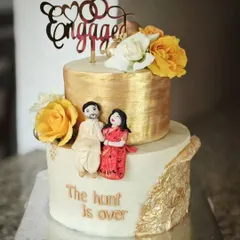 "The hunt is over!" This stunning two-tier engagement cake is decorated with gold leaf, fresh flowers, and a personalized fondant couple. It's a delicious butter chocolate sponge with hazelnut filling.