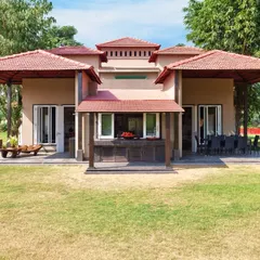The front facade of the Aishbagh cottage, showcasing its symmetrical design and layered, sloped roofs with terracotta tiles. The architecture is designed to feel organic and rooted in its natural environment.