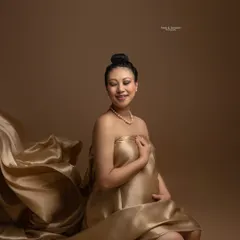 Wrapped in liquid gold. This stunning portrait uses flowing satin fabric to create a regal and elegant look, highlighting the beauty and serenity of this special time against a warm, earthy backdrop.