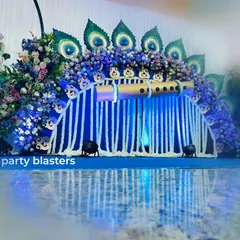 A full view of my popular Krishna-themed naming ceremony decor. The setup features a custom-built backdrop with a large flute, peacock feather details made from natural materials, and a cascade of white tuberose garlands, creating a divine and vibrant setting for the celebration.