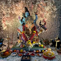 An elegant and serene home Ganpati setup featuring a beautiful idol of Ganesha with Shiva and Parvati. The backdrop is a dense wall of delicate white blossoms, creating a heavenly and peaceful ambiance for prayer and offerings.