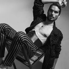 A black and white editorial shot featuring a model in a pinstripe suit styled with a leather corset. This look pushes the boundaries of traditional menswear, creating a bold, androgynous, and high-fashion statement.