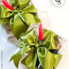 Modern and chic return favors in clear acrylic boxes. The contents are visible, and the gift is finished with a voluminous olive green satin bow and a single red dried flower for a touch of color.