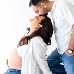 An intimate moment between expecting parents, captured in a bright, minimalist studio setting. This candid couple's pose highlights the connection and joy of pregnancy.