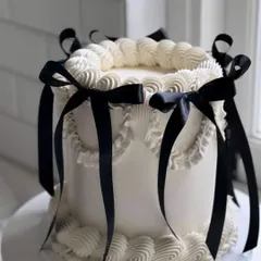 A classic white buttercream cake gets a touch of drama with elegant black ribbons. This vintage-inspired "coquette" cake is perfect for a chic and sophisticated celebration where style is key.