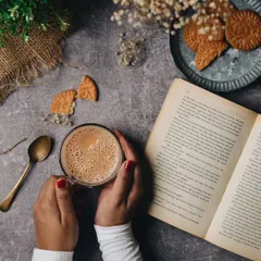 Curled up with hot coffee and a good book in this cozy rainy weather. This top-down shot captures a perfect moment of peace and contentment, with rustic props to enhance the mood.
