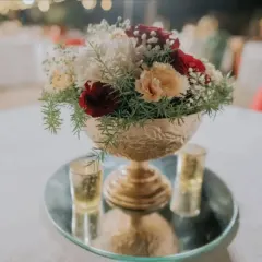A close-up of a classic floral centerpiece in a golden bowl. The mix of red, white, and peach roses with baby's breath is a timeless combination that adds elegance to any table setting.
