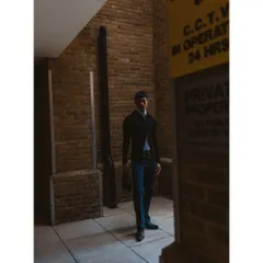 A full-length shot in an urban alleyway. The composition uses the surrounding walls and signs to frame the model, creating a gritty and atmospheric menswear editorial image.