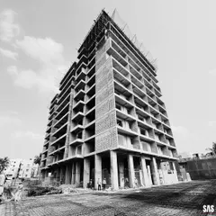 A low-angle shot of the JP Nagar project under construction emphasizes its powerful, monolithic form. The raw concrete and blockwork reveal the building's skeleton, showcasing the structural clarity and intentional design that will define the finished facade.