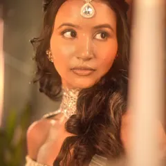 A close-up portrait from the same shoot, with dramatic, warm lighting. The makeup is designed to look flawless and glowing on camera.