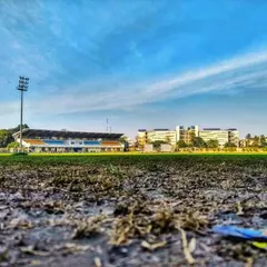 The ground tells a story of hard-fought battles. A worm's-eye view of the cricket pitch, with the main pavilion standing tall in the background.