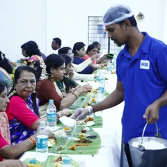 Our professional server, in full uniform with a hairnet and gloves, carefully serves rice to guests during a traditional banana leaf service, ensuring hygiene and attentiveness.