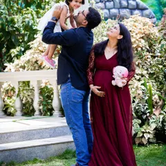 A joyful, candid moment during a family maternity session. The father lifts his daughter high as the mother-to-be looks on with a smile, capturing the happiness of a growing family.