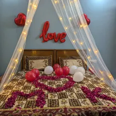 A close-up of the bed decor, with a heart shape made from rose petals, a 'love' foil balloon, and a fairy light canopy.