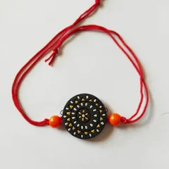 This rakhi features a delicate spiral pattern in white and yellow on a black base. It's a simple yet striking design, attached to a traditional red thread.