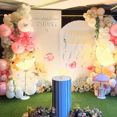 A dreamy butterfly garden party for a second birthday, with a custom two-panel backdrop personalized with the name "Nawal". The decor includes soft balloon arches, glowing flower and mushroom props, and a faux grass floor for an immersive garden feel.