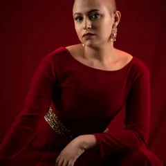 A direct and striking portrait. The makeup features a defined brow, subtle eye contour, and a deep red lip, creating a look that is both elegant and fierce.