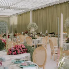 An overview of the dining setup, showing the elegant table arrangements under a striped canopy. The soft green draping and abundance of fresh flowers create a serene and sophisticated ambiance for the luncheon.