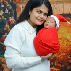 A mother holds her newborn baby, both dressed for a festive Christmas-themed photoshoot. We love creating special holiday memories for your family's firsts.