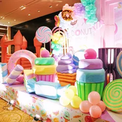 A full view of the Candyland stage area, showcasing a variety of large, custom made props including cupcakes, ice cream cones, and candy swirls. A pink bouncy castle is visible in the background, integrated into the decor.