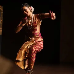A dynamic action shot from a live performance. The posture captures the energy and movement of Bharatanatyam, highlighting the physical demands and grace of the art form.